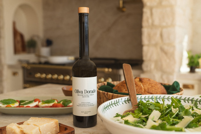 A bottle of Oliva Dorado olive oil on a kitchen counter with salad and fresh bread